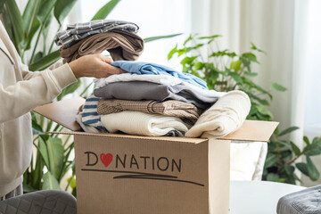 Donation concept. A woman puts clothes in a cardboard box at home for donation