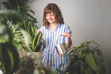 A young woman enjoys caring for flowers. Watering indoor plants and admiring them.