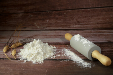 pile of flour together with a rolling pin and some ears of wheat on a wooden table and copy space