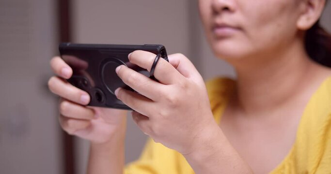 Clutching a digital mobile phone with both hands as the woman is playing and browsing some games and the social media on the internet.
