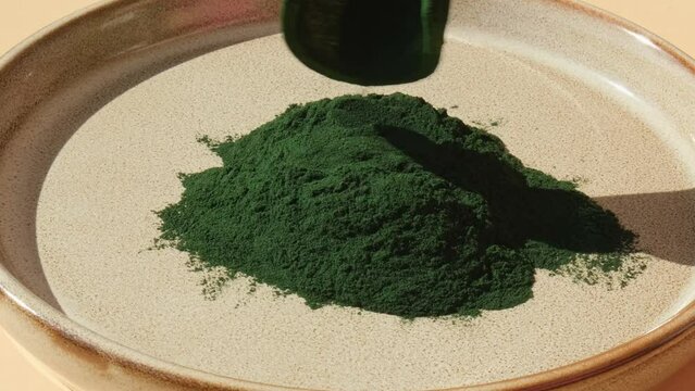 Natural organic green spirulina algae powder in plate and wooden spoon on neutral background. Chlorella seaweed vegan superfood supplement source and detox. Copy space Healthy nutritional antioxidant