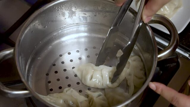 A cooking chef uses a metal grabber to retrieve dumplings from a metal bowl, epitomizing the art of culinary preparation and food crafting.