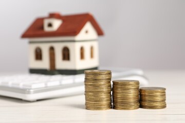 Mortgage concept. Stacks of coins, model house and calculator on white wooden table, selective focus