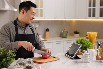 Fototapeta na wymiar Cooking process. Man using tablet while cutting fresh bell pepper at countertop in kitchen