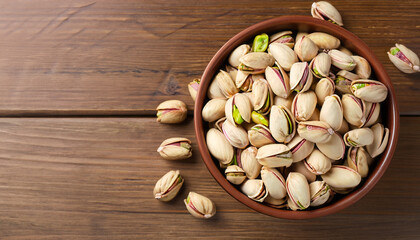 Delicious pistachios in bowl on wooden table. Space for text