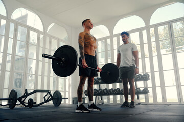 Two fit multiracial young men in sports clothing doing weight training at the gym