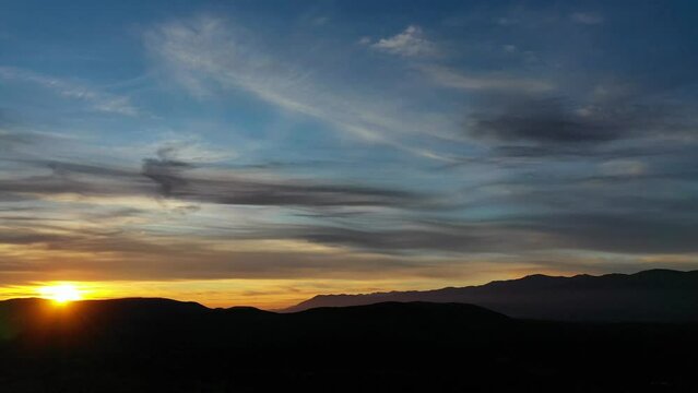 flight in a sunset in a valley with a mountain system of dark almost black color with a yellow, blue sky and with gray clouds and the sun setting in the mountains watching it with a twist in Spain