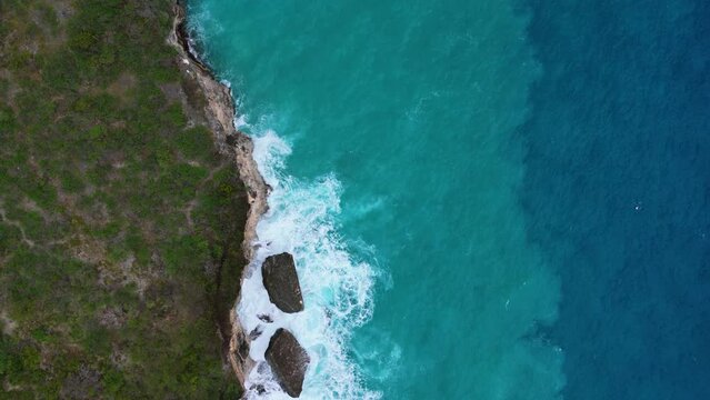 Drone top down pan across Caribbean island coastline with sand in undertow and deep blue drop off, bird's eye view