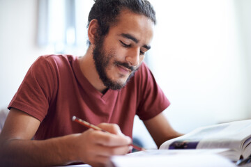 University, student and man reading textbook for education with scholarship, smile and studying. Male person, happy and learning for information with research on table or desk of classroom in academy