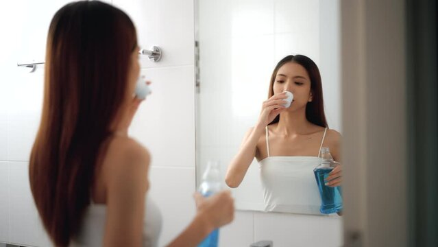 Young asian woman is gargling with a blue mouthwash for good dental health and fresh bad breath at basin in the bathroom.
