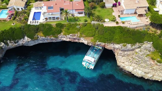 Pedestal descending drone shot of Cala Anguila, revealing some residential mansions and guest houses above an underground cave located in the island of Mallorca.