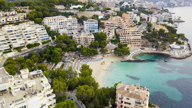 Playa illetas with clear waters, beach-goers, and surrounding buildings on a sunny day, drone shot, aerial view