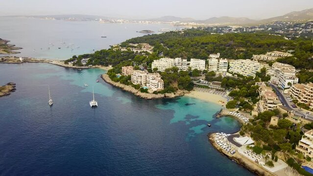 Playa illetas with clear turquoise waters and anchored yachts, surrounded by greenery and resorts, aerial view