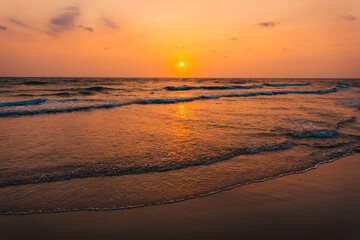 Fototapeta na wymiar Sunset on the beach and orange sea waves