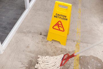Caution wet floor sign positioned on a concrete surface next to a mop, indicating a freshly cleaned or slippery area.