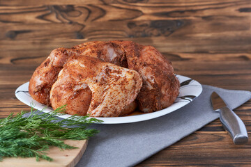 Chicken in marinade on white plate with dill on wooden background. Tobacco chicken