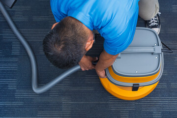 A janitor attaches the soft tube to a commercial grade wet and dry vacuum cleaner on the carpeted...