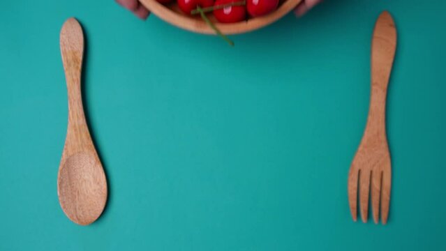 wooden bowl filled with cherries between a wooden spoon and fork isolated blue background