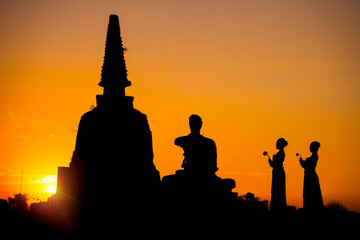 Silhouette women take flowers come to respect buddha and ancient pagoda in temple at sunset time.