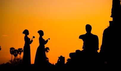 Silhouette women take flowers come to respect buddha and ancient pagoda in temple at sunset time.