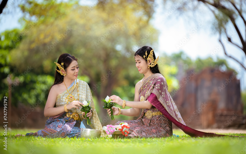 Wall mural Asian woman wearing ancient Thai traditional dress holds garland and fresh flowers paying homage Buddha in temple to make a wish on the traditional Songkran festival in Thailand.