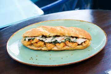 Close-up of a sub sandwich with egg, meat, and vegan on a green plate and on a wooden table