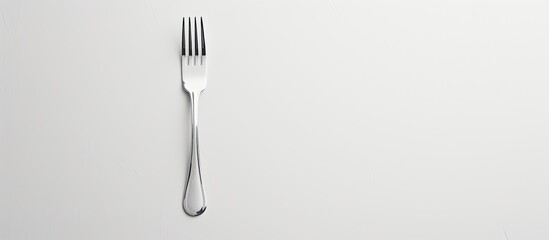 A small silver fork with two prongs rests on a white surface against a white background.