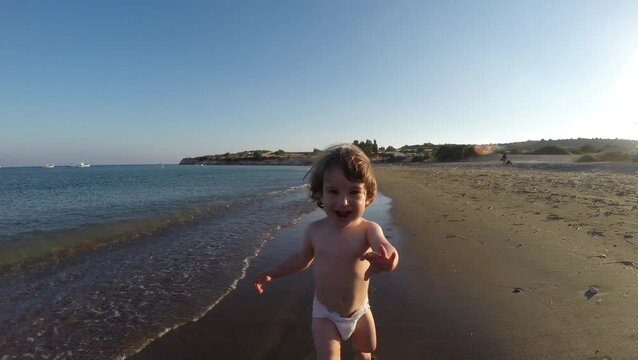 Slow motion of toddler baby girl in nappy running on sandy beach through sea waves