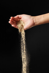 Hand sprinkling ground pepper on black background