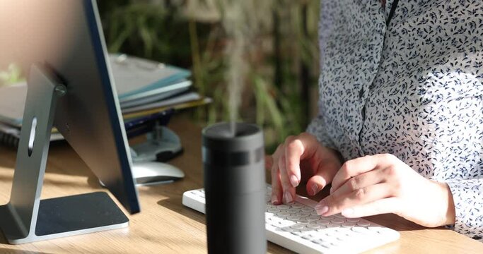 Businesswoman working on computer keyboard near portable air humidifier closeup 4k movie slow motion. Household appliances to create comfortable microclimate in room concept