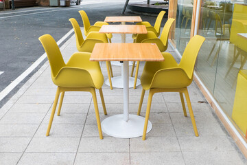 Yellow steel chairs and tables near street in city, empty with nobody using the area,restaurant or cafe.