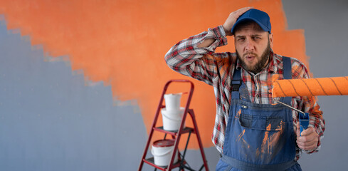 Painter man holding a paint roller on wall background with headache and problem on the workplace.