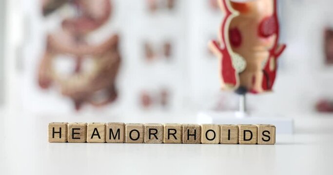 Word hemorrhoids on wooden cubes on background of model of rectum and poster 4k movie. Diagnosis and treatment of diseases of rectum concept