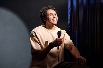 Young cheerful male comedian with microphone in hand performing new monologue in front of audience...