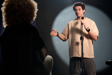 Young man in t-shirt speaking in microphone and looking at audience or group of judges during...