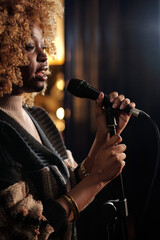 African American female comedian with microphone standing on stage in front of audience while...