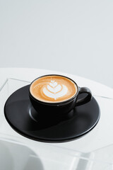 A cup of coffee with latte art in a black cup on white table background