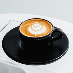A cup of coffee with latte art in a black cup on white table background