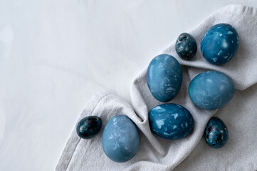 Creative naturally dyed blue Easter eggs on white marble tabletop and linen napkin, traditional holiday Easter food, aesthetic minimalist Scandinavian style