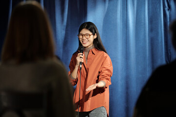Happy young female participant of stand up show pronouncing monologue in microphone and looking at...