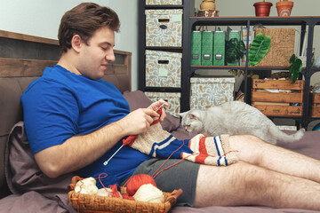 Young man knitting a striped sweater at home.