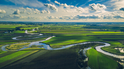 Drone landscape of green fields and meadows, as well as meanders of the Prosna River in Poland on a beautiful sunny spring day with blue sky and clouds - obrazy, fototapety, plakaty