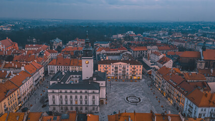 Fototapeta na wymiar illuminated night view of the town hall in Kalisz, Poland from a drone, dramatic blue sky before rain, view of old tenement houses and architecture