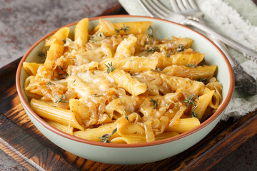 Delicious French onion pasta penne with caramelized onions, fragrant thyme, garlic and gruyere cheese close-up on a bowl on a wooden board. Horizontal