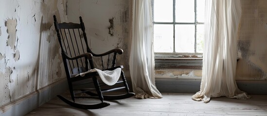 An old, weathered black rocking chair sits in front of a window, exuding vintage charm and character. The chair invites relaxation and contemplation as it gently rocks against the backdrop of natural