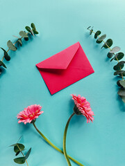 A pink envelope is seen resting on top of a blue table with pink gerbera flowers.