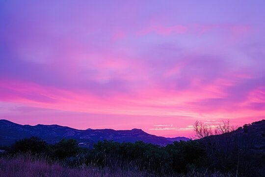 A stunning photo capturing the beauty of a pink and purple sky as it stretches over a majestic mountain range in the background, Shades of pink and purple blending in the sunset, AI Generated