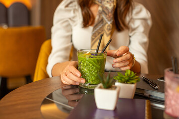 Woman hand holding glass of a green smoothie in the restaurant