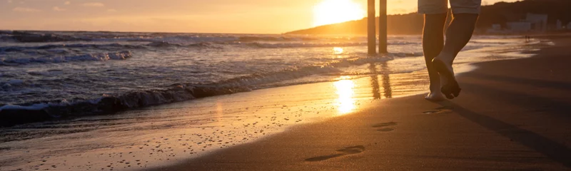 Fotobehang Web banner 4x1. The incoming waves on the sandy beach at sunset. A sunny path. Bare footprints © Anna