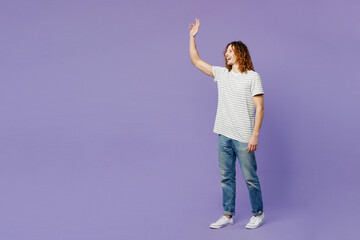 Full body side view smiling young man he wears grey striped t-shirt casual clothes waving hand say hi hello walk go isolated on plain pastel light purple background studio portrait. Lifestyle concept.
